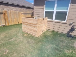 Wooden enclosure around an outdoor air conditioning unit, next to a house and a wooden fence.