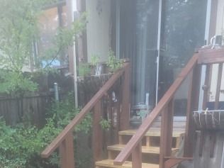 Wooden stairs with handrails leading to a sliding glass door. Green plants are visible.