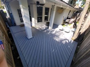 Gray composite deck with white columns, overlooking a backyard.
