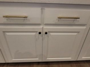 White kitchen cabinets with gold drawer pulls and black door knobs.