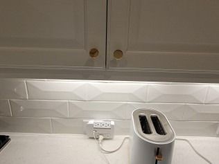 White kitchen: toaster plugged into an outlet on the backsplash, under white cabinets with gold knobs.