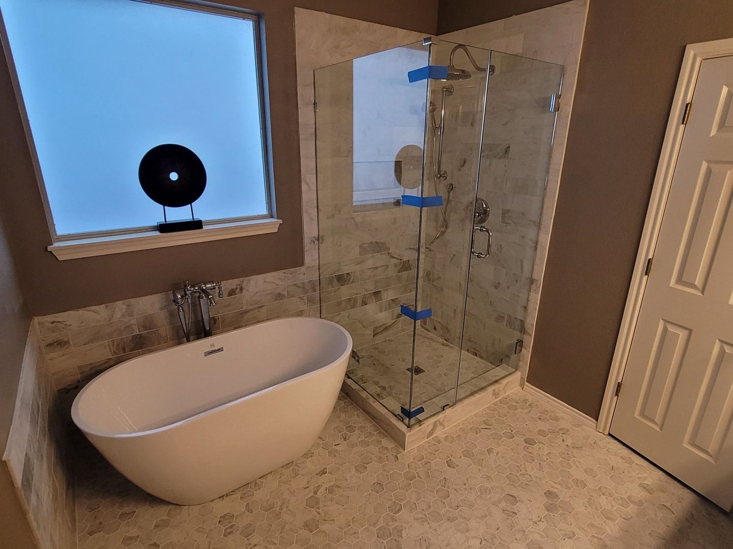 Modern bathroom with white tub, glass shower, and marble-look tile.
