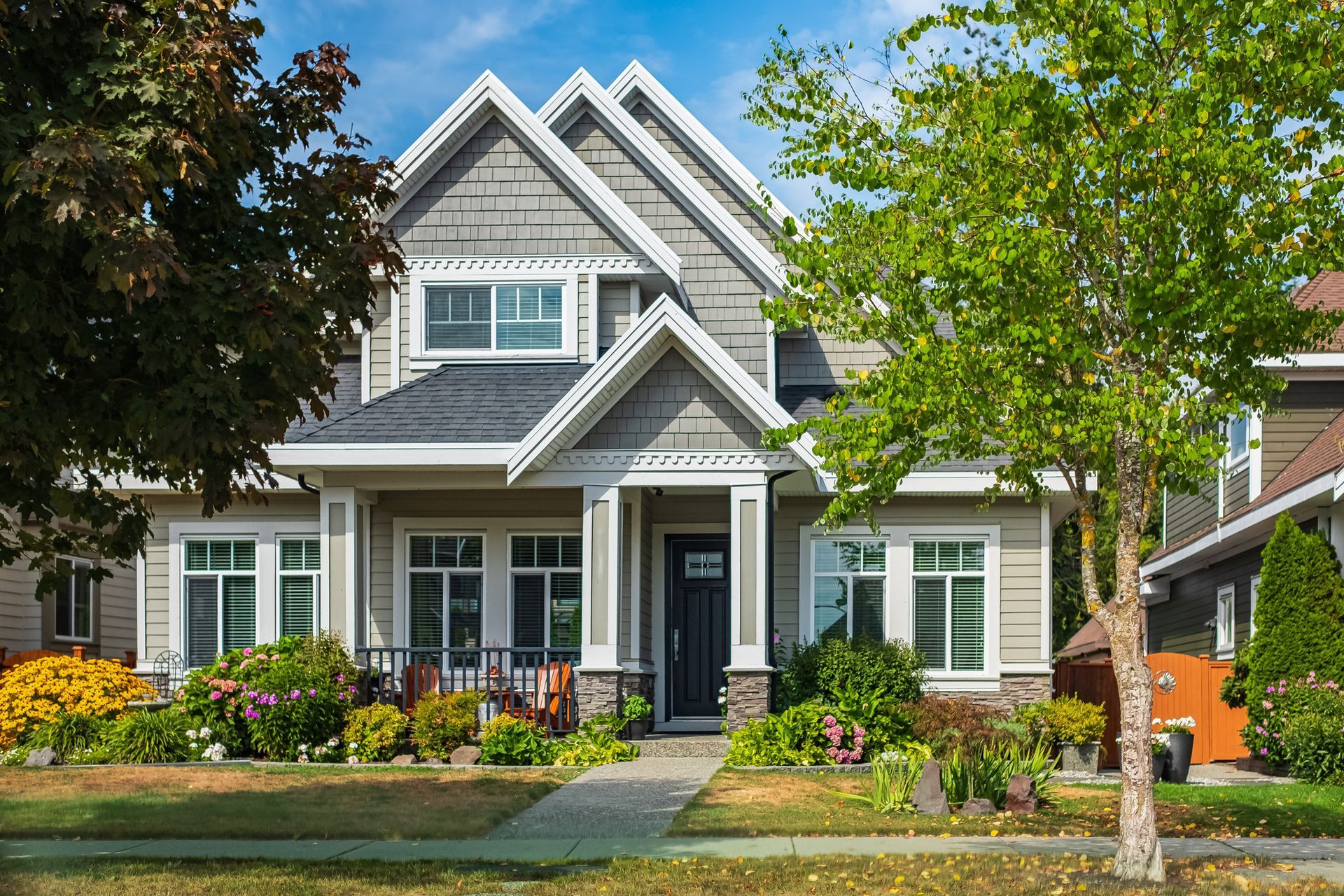 Two-story house with light gray siding, white trim, black front door, and a well-manicured front yard.