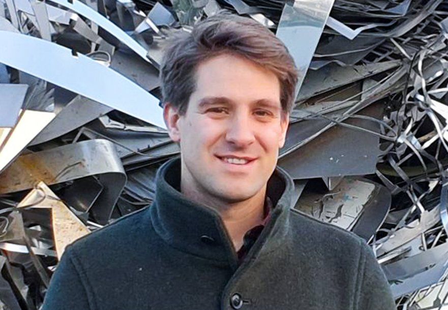Philipp Rüschen in einem grauen Mantel steht vor einem Metallhaufen.
