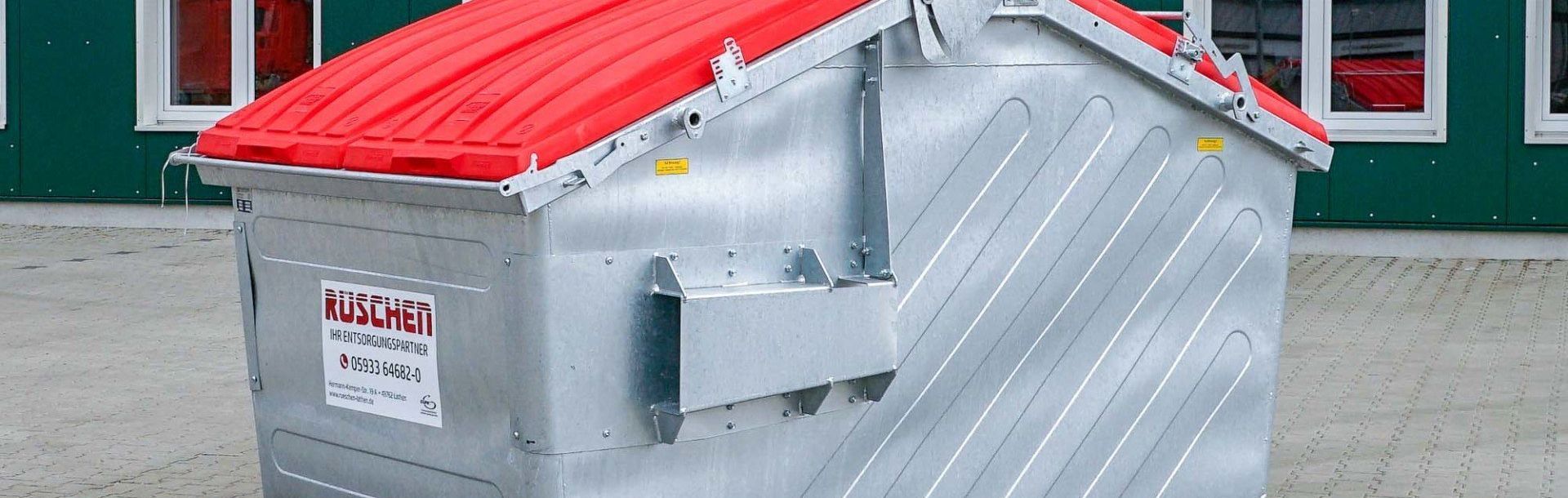 Vor einem Gebäude steht ein Müllcontainer mit rotem Dach.