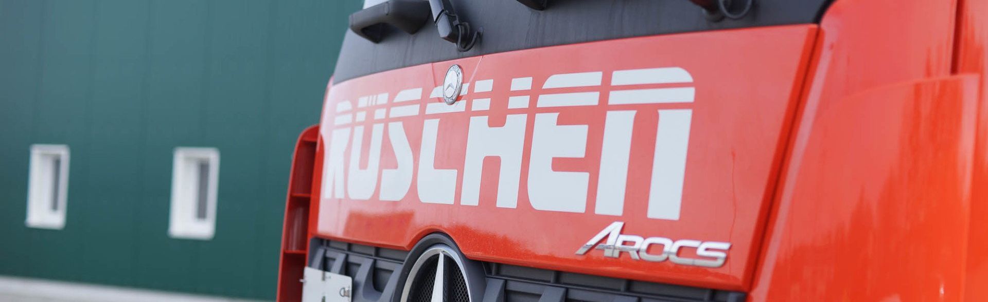 Ein roter Lastwagen parkt vor einem grünen Gebäude.