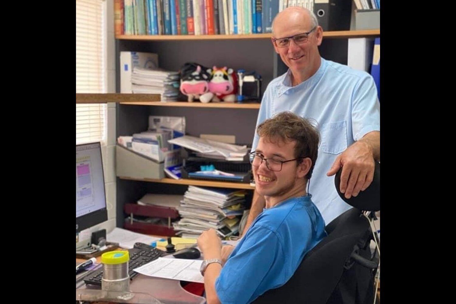 A man is standing next to a man sitting at a desk in front of a computer — Barry Bennett Dental In Earlville, QLD