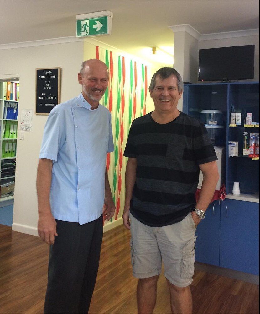 Two Men Standing Next To Each Other In A Room With A Green Exit Sign Above Them — Barry Bennett Dental In Earlville, QLD