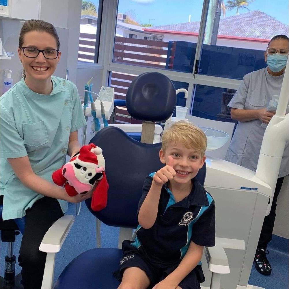 A Young Boy Is Sitting In A Dental Chair Holding A Stuffed Animal — Barry Bennett Dental In Earlville, QLD