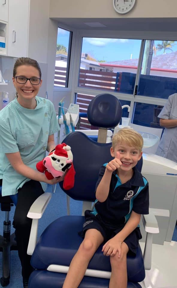 A woman is sitting next to a young boy in a dental chair holding a stuffed animal — Barry Bennett Dental In Earlville, QLD