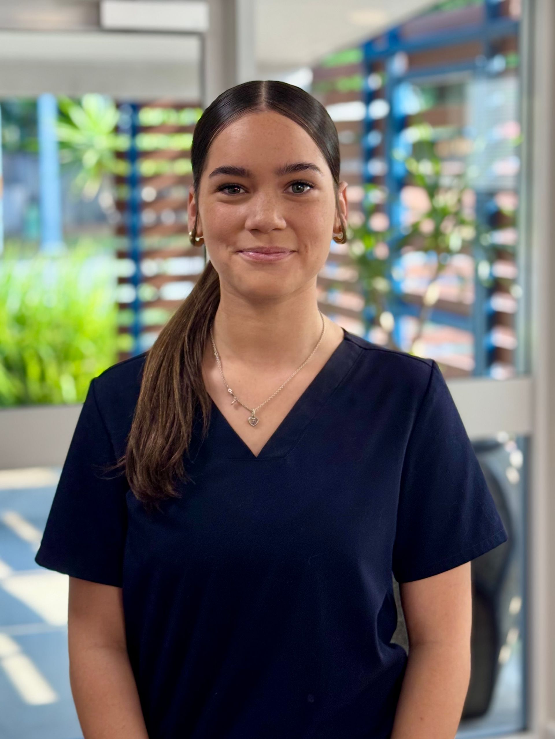 Woman in dark blue scrubs smiles, standing indoors.