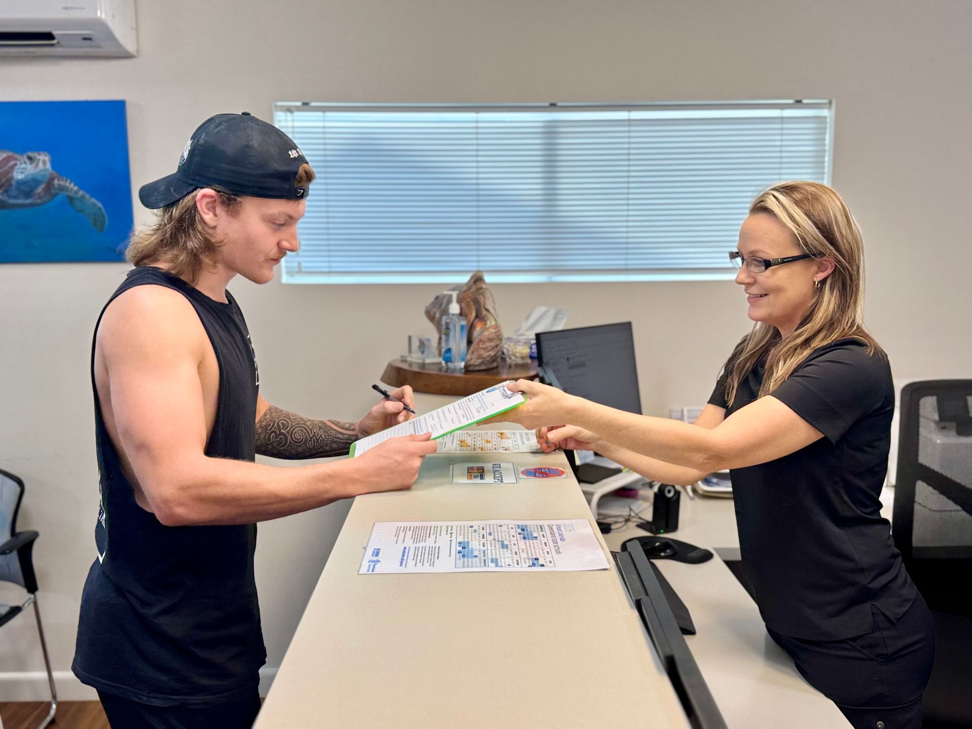 Man signing paperwork at a desk, handing it to a woman in a reception area.