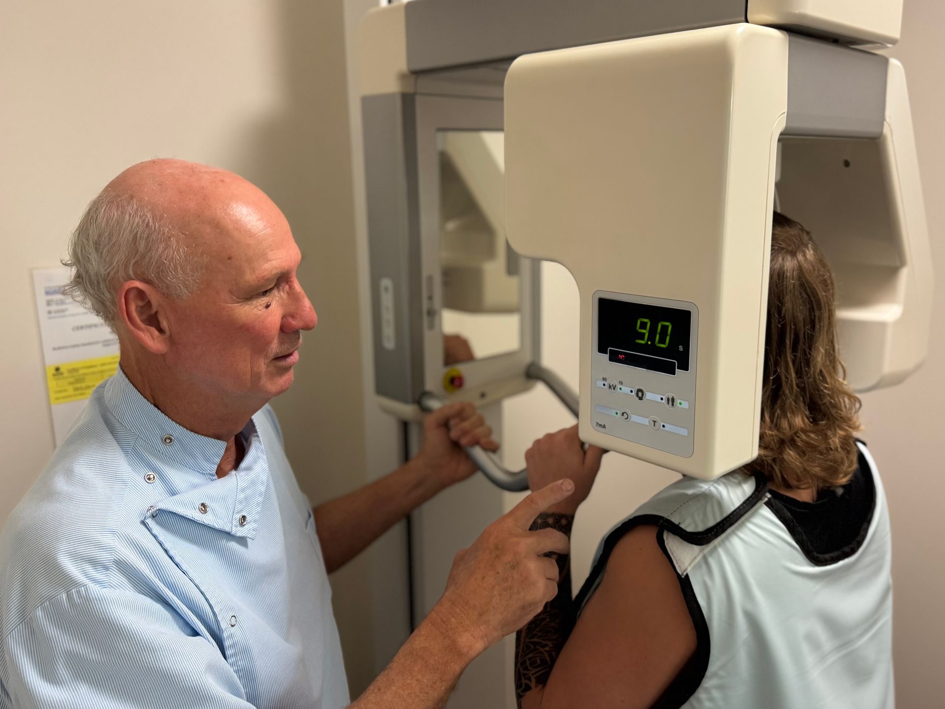 Dentist adjusting a patient's head in a panoramic X-ray machine; patient wears a protective vest.