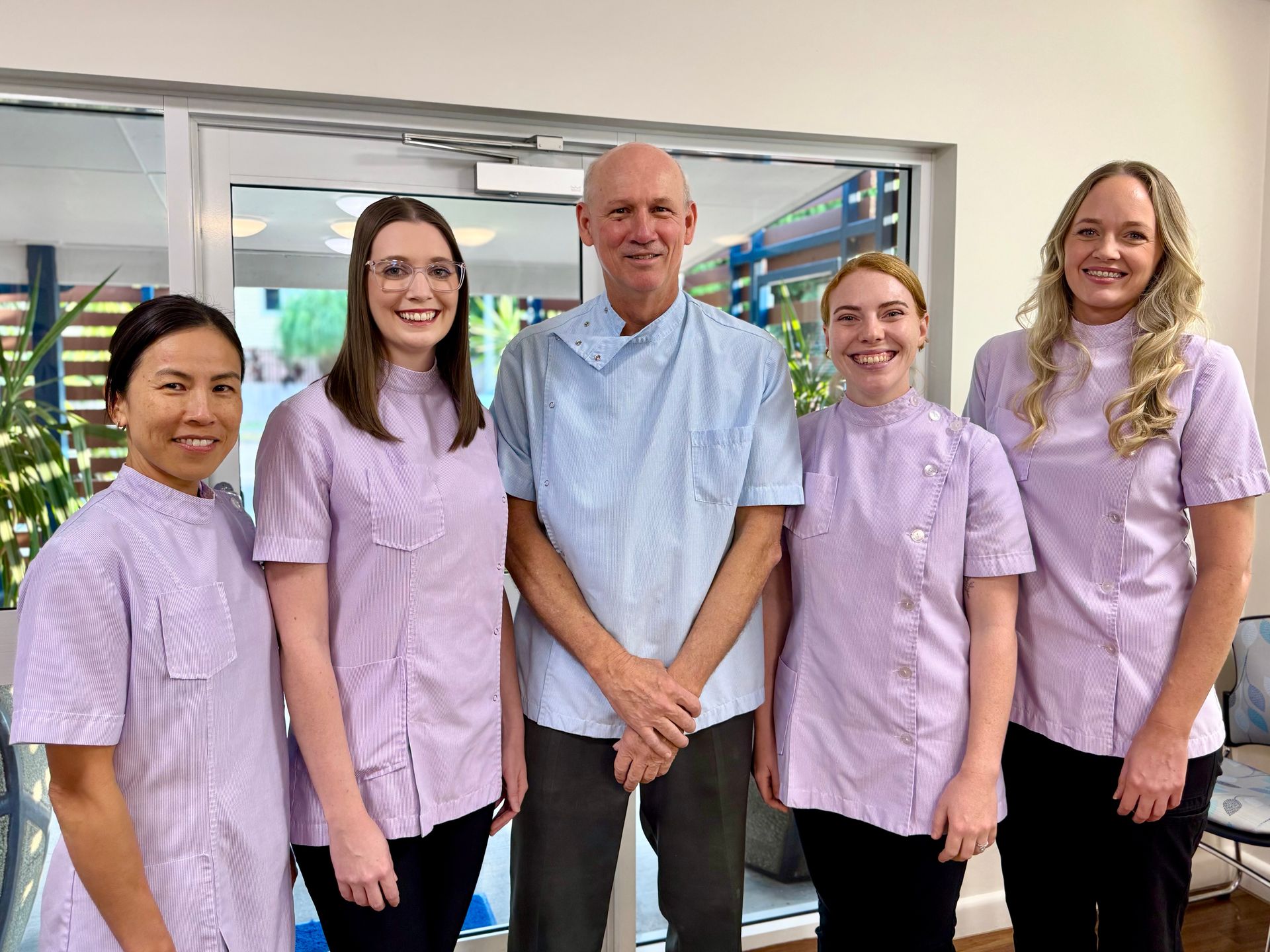 Five people in dental scrubs pose together in a light-filled office.