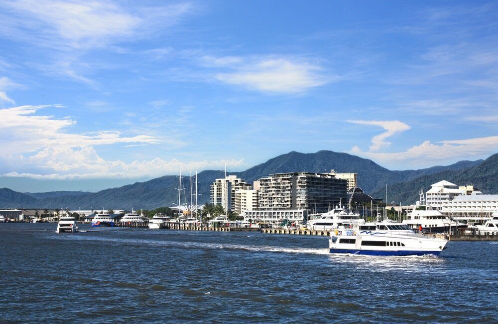 A Boat Is Floating In The Water Near A City With Mountains In The Background — Barry Bennett Dental In Cairns, QLD