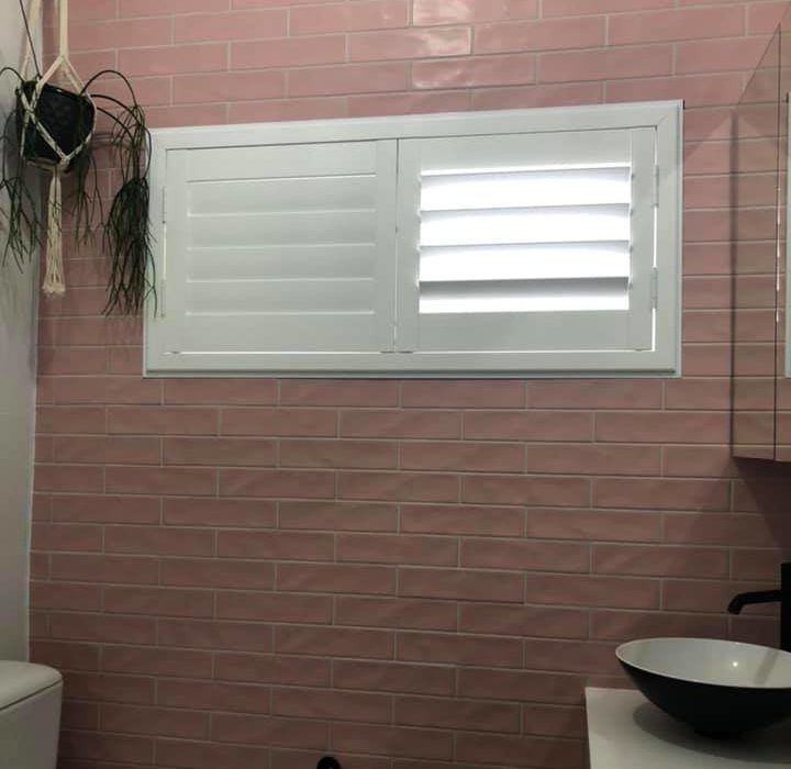A Bathroom with Pink Tiles , a Sink , and A Window with White Shutters — Bay Blinds & Doors in Bateau Bay, NSW