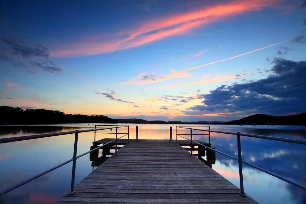 There is a dock in the middle of a lake at sunset - Bay Blinds & Doors in Kincumber, NSW