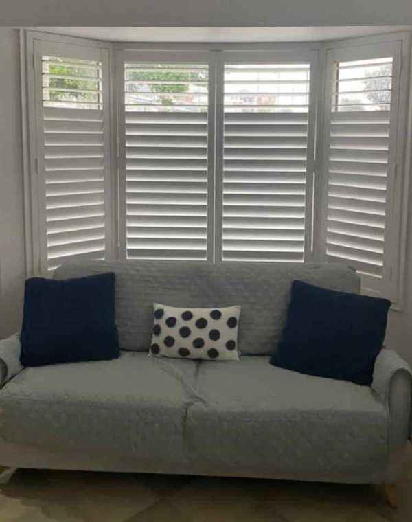 A Couch Is Sitting in Front of A Window with Shutters — Bay Blinds & Doors in Berkeley Vale, NSW