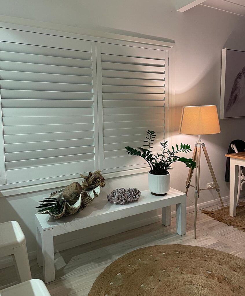 A Living Room with White Shutters , a Lamp , and A Bench — Bay Blinds & Doors in Bateau Bay, NSW