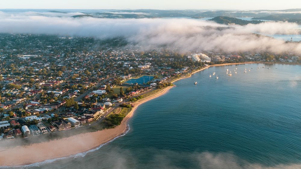 An aerial view of a city surrounded by water and clouds — Bay Blinds & Doors in Umina Beach, NSW