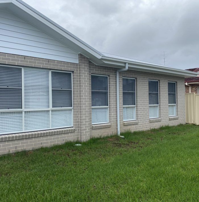 A Brick House with A Lot of Windows and Blinds on It — Bay Blinds & Doors in Umina Beach, NSW