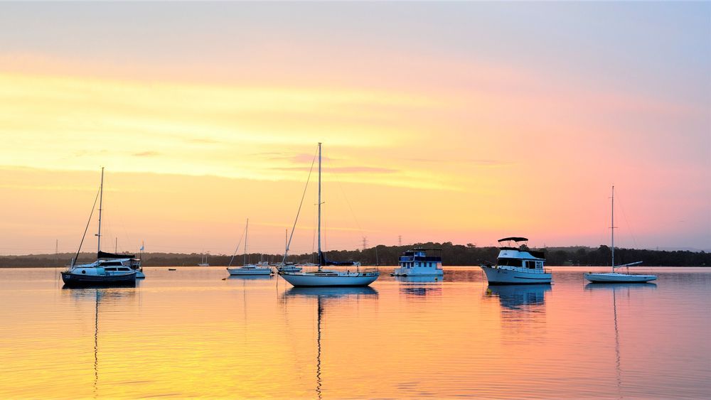 A group of boats are docked in the water at sunset — Bay Blinds & Doors in Wyee, NSW