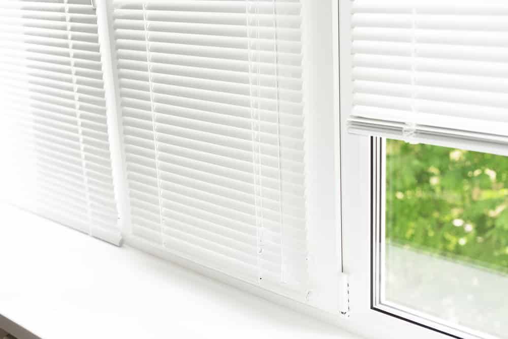 A Close up Of a Window with White Blinds on It — Bay Blinds & Doors in Bateau Bay, NSW