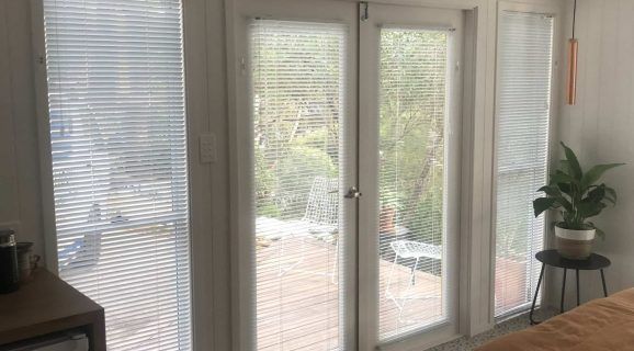 A Gray and White Striped Roman Shade Is Hanging on A Window — Bay Blinds & Doors in Erina, NSW