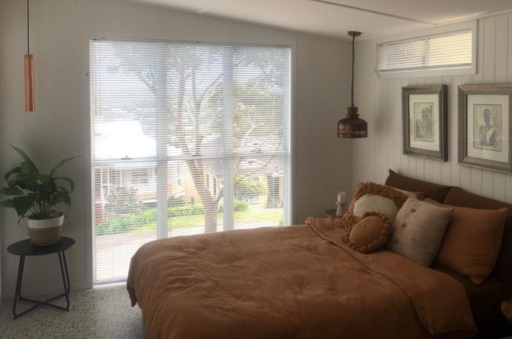 A Gray and White Striped Roman Shade Is Hanging on A Window — Bay Blinds & Doors in Morisset, NSW