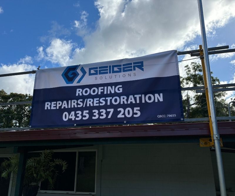 A Banner for Roofing Repairs and Restoration Hangs From a Scaffolding on Top of a Building — Geiger Solutions In Mackay, QLD