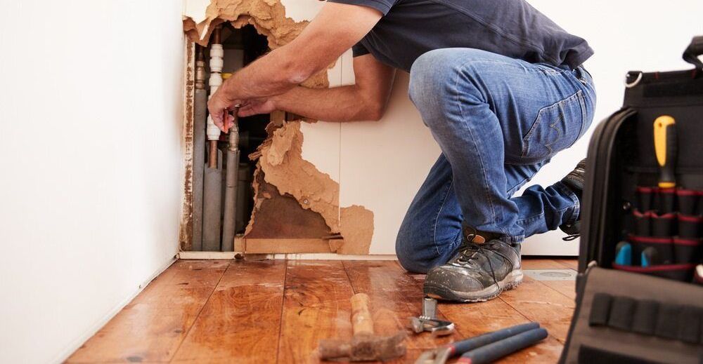 A Man is Kneeling on the Floor Fixing a Hole in the Wall — Geiger Solutions In Clermont, QLD