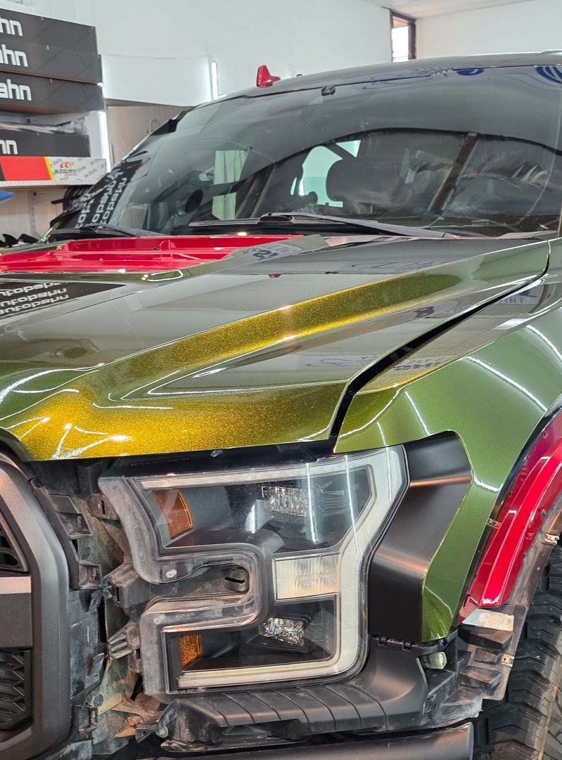 Ford Raptor truck with green and gold paint, red accents, inside a shop.