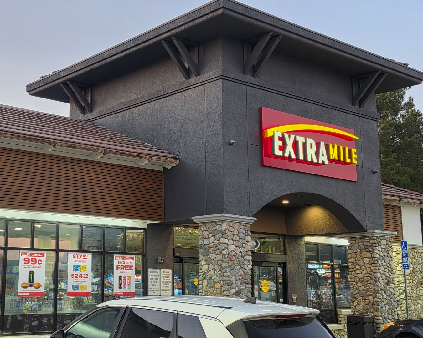 Exterior of an Extra Mile gas station. The sign is red and yellow. The building has stone pillars. A car is parked out front.