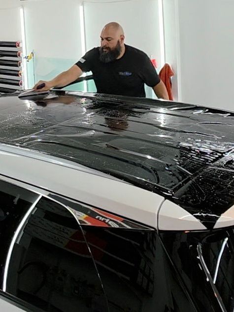 A man is wrapping the roof of a car in a garage.