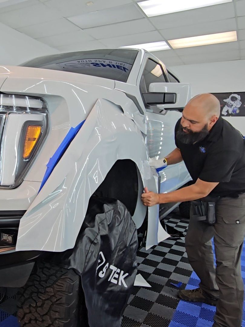 A man is wrapping the fender of a white truck.