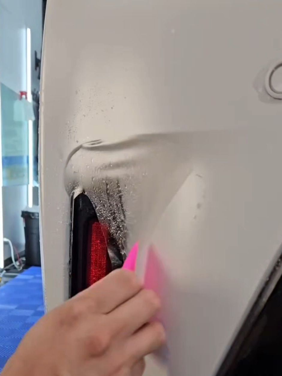 A person is wrapping a car with a pink squeegee.