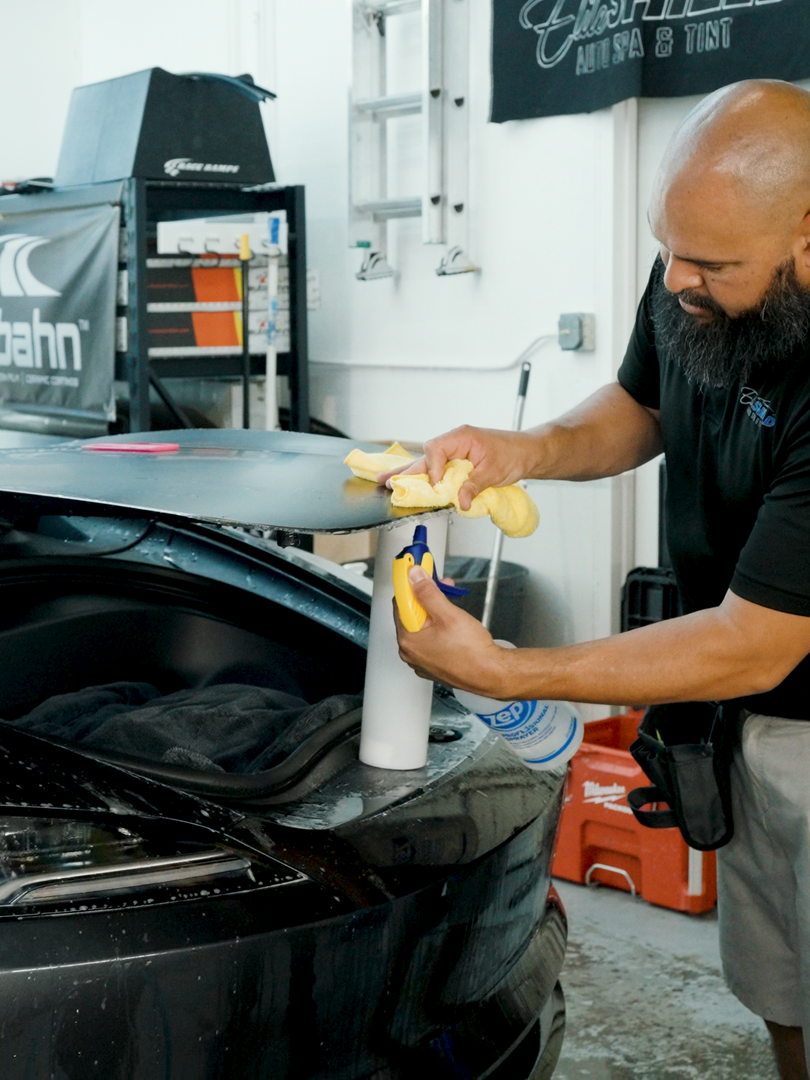 A man with a beard is cleaning a car with a spray bottle