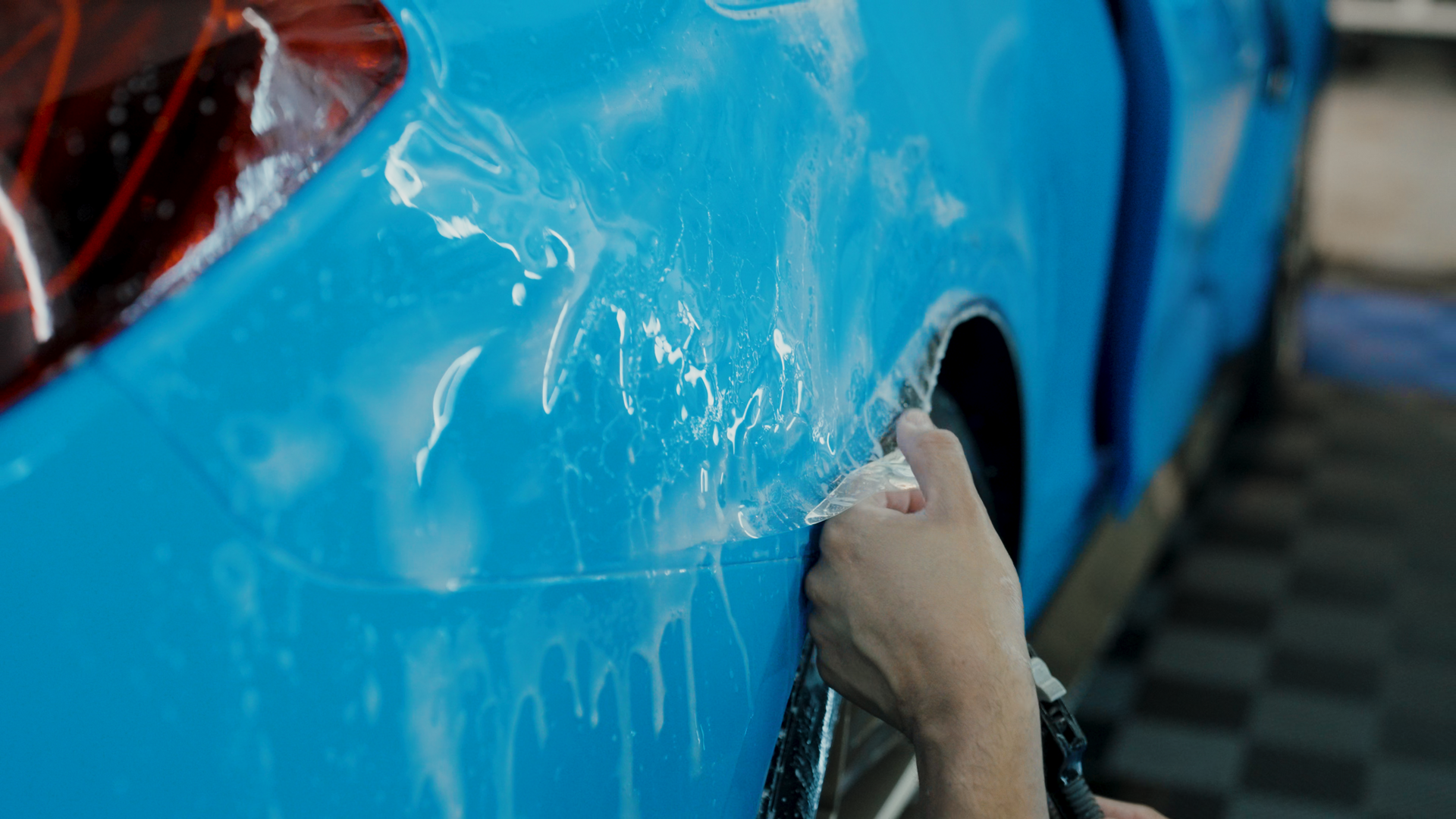 A person is wrapping a blue car with plastic wrap.