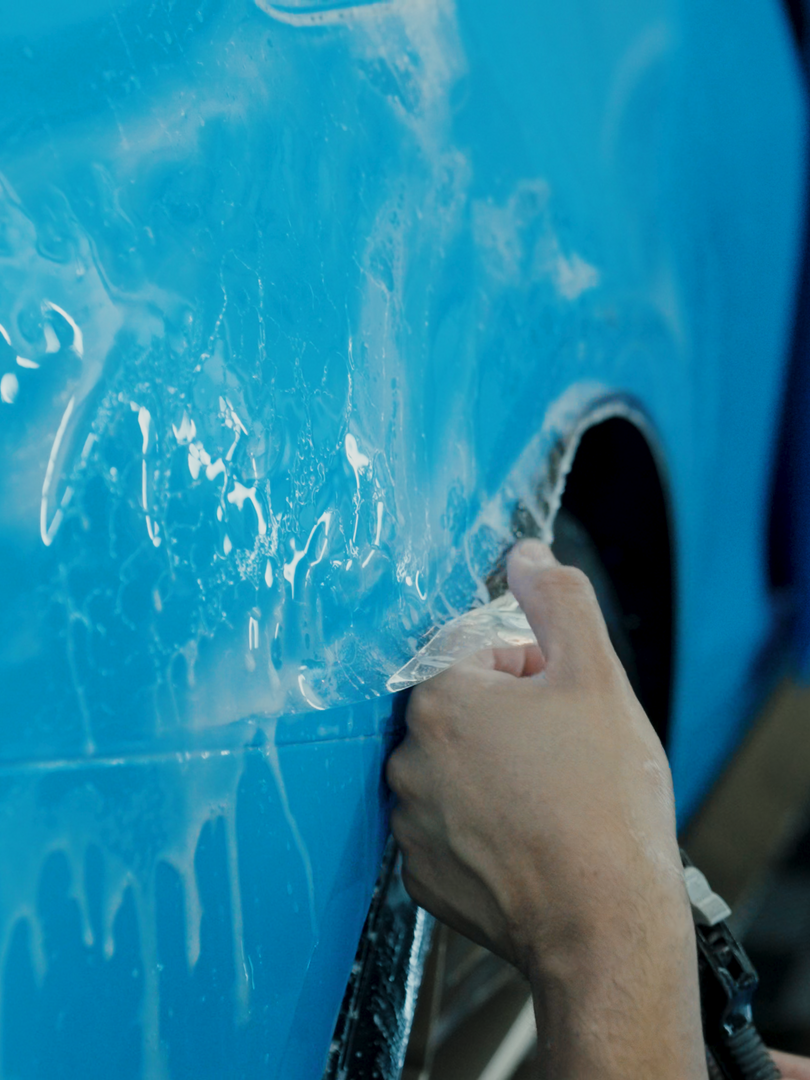 A person is cleaning a blue car with a brush.