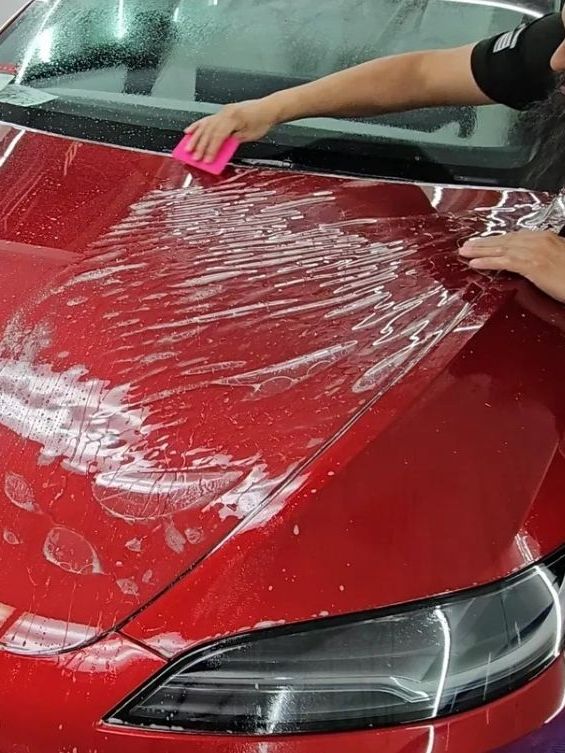 A person is cleaning the hood of a red car with a sponge.
