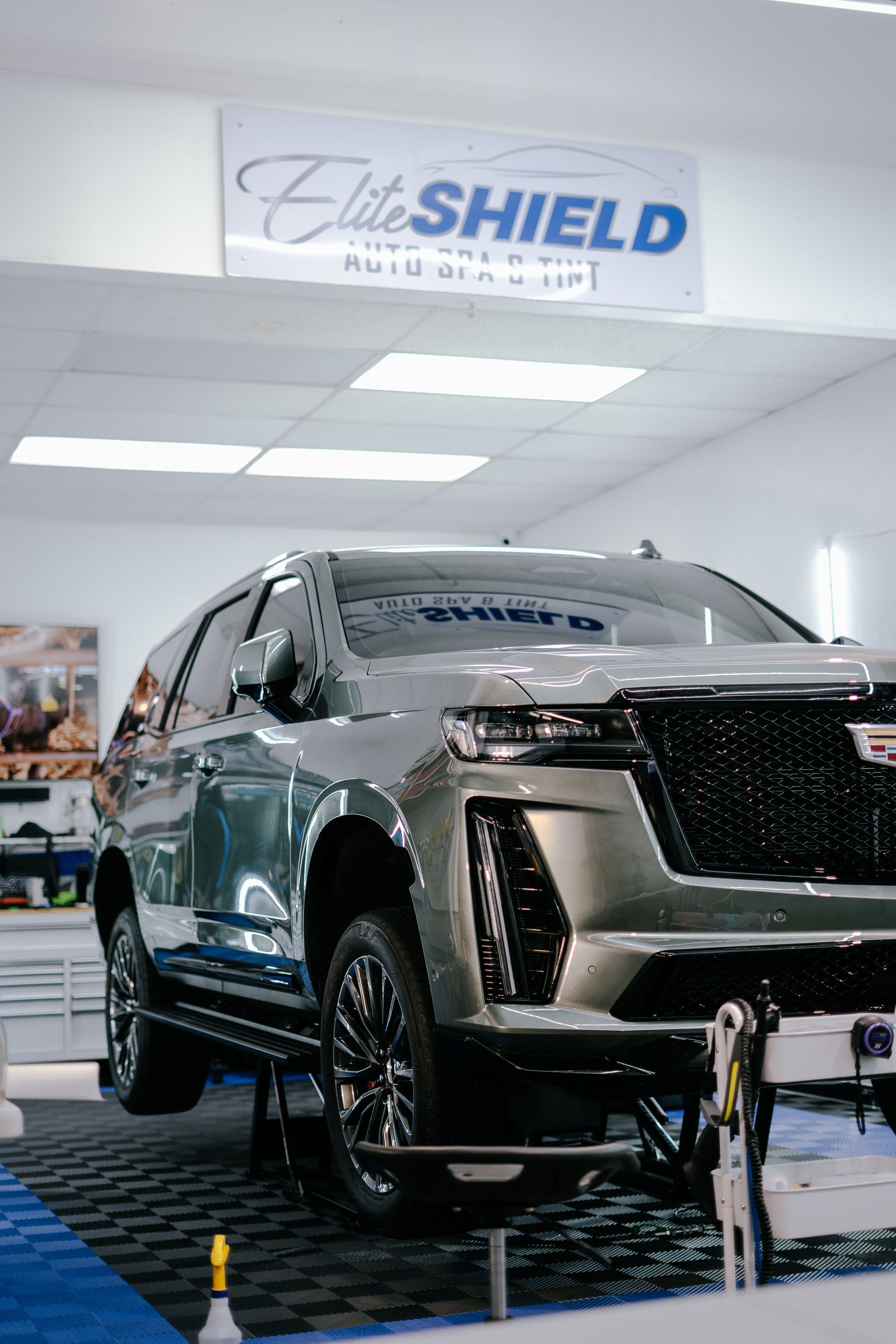 A cadillac escalade is sitting on a lift in a car wash.