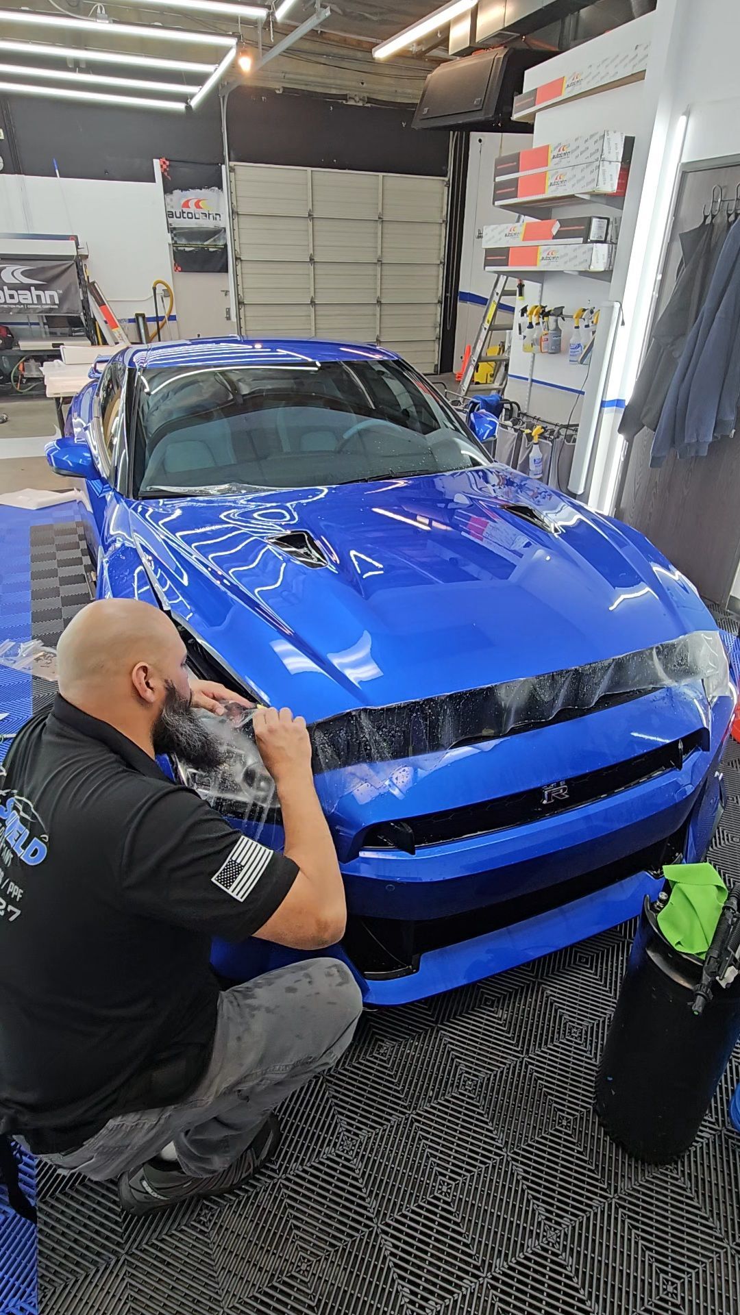 A man is kneeling down next to a blue car in a garage.
