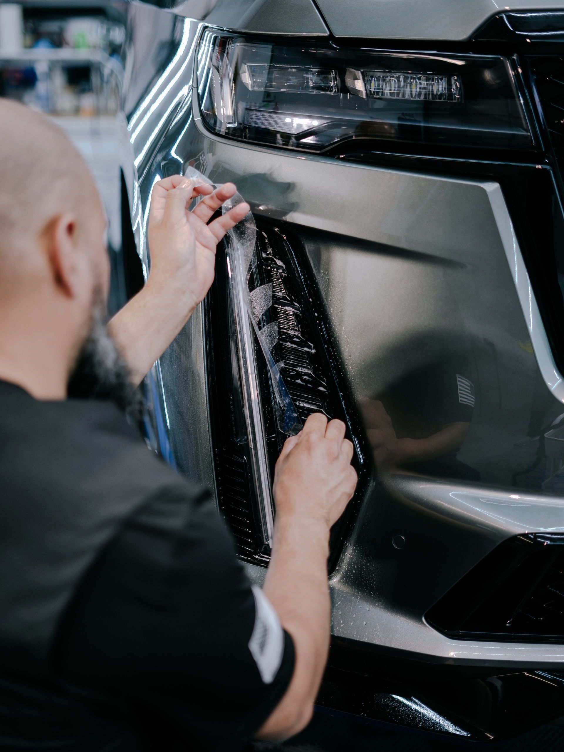 A man is applying a protective film to the front of a car.