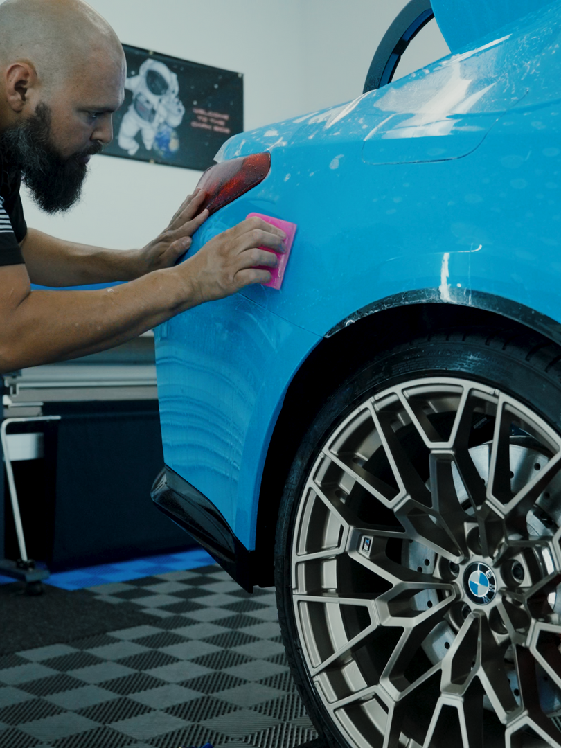 A man is cleaning a blue car with a pink sponge