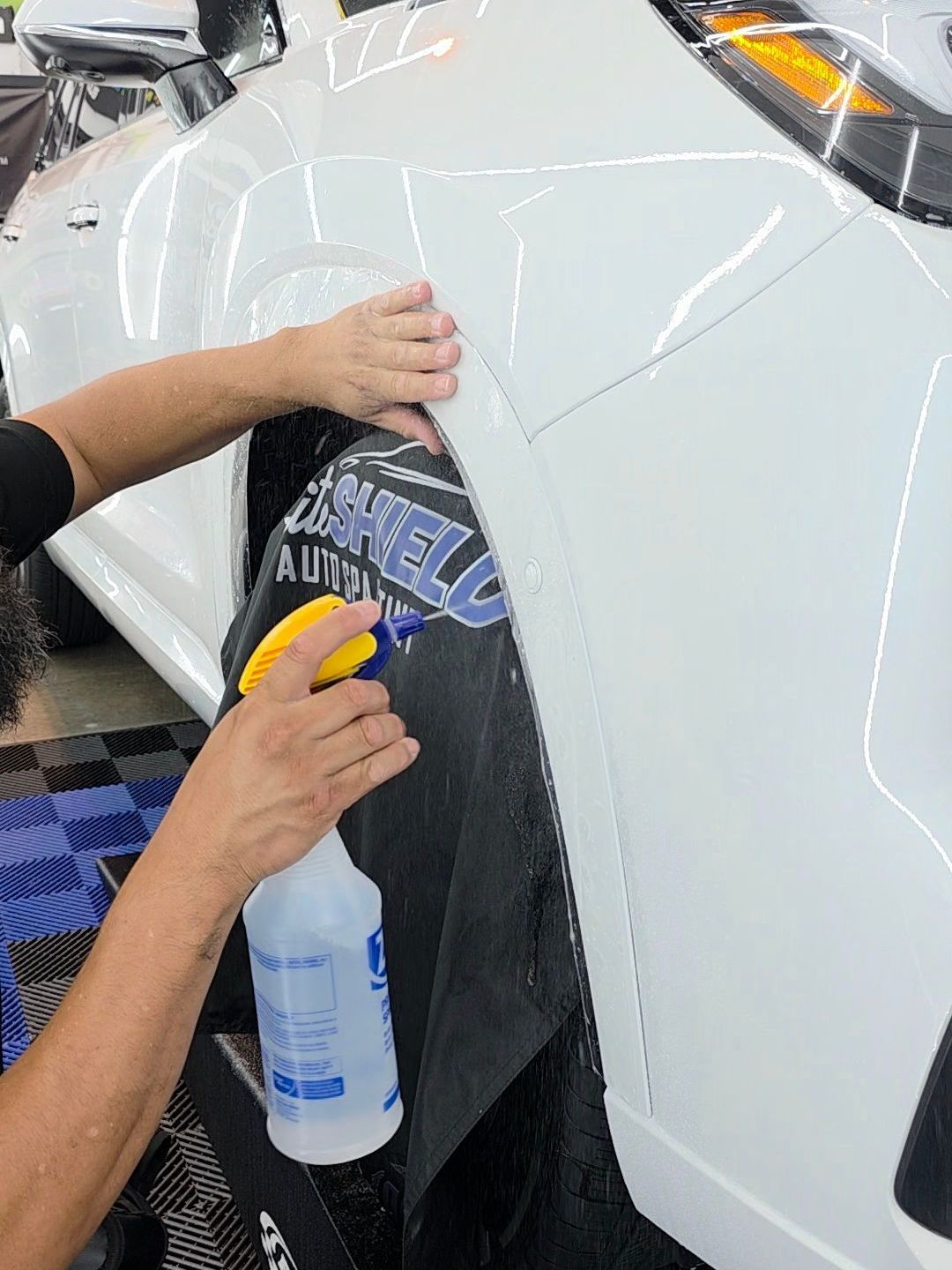 A man is applying a film to the fender of a white car.