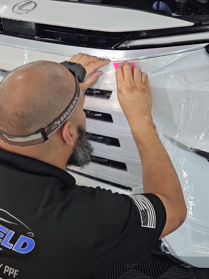 A man is wrapping the front of a car in plastic.
