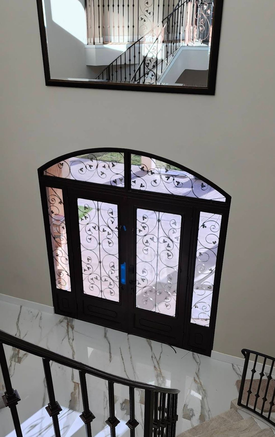 Door with decorative glass, below a mirror and a staircase with wrought iron railing.