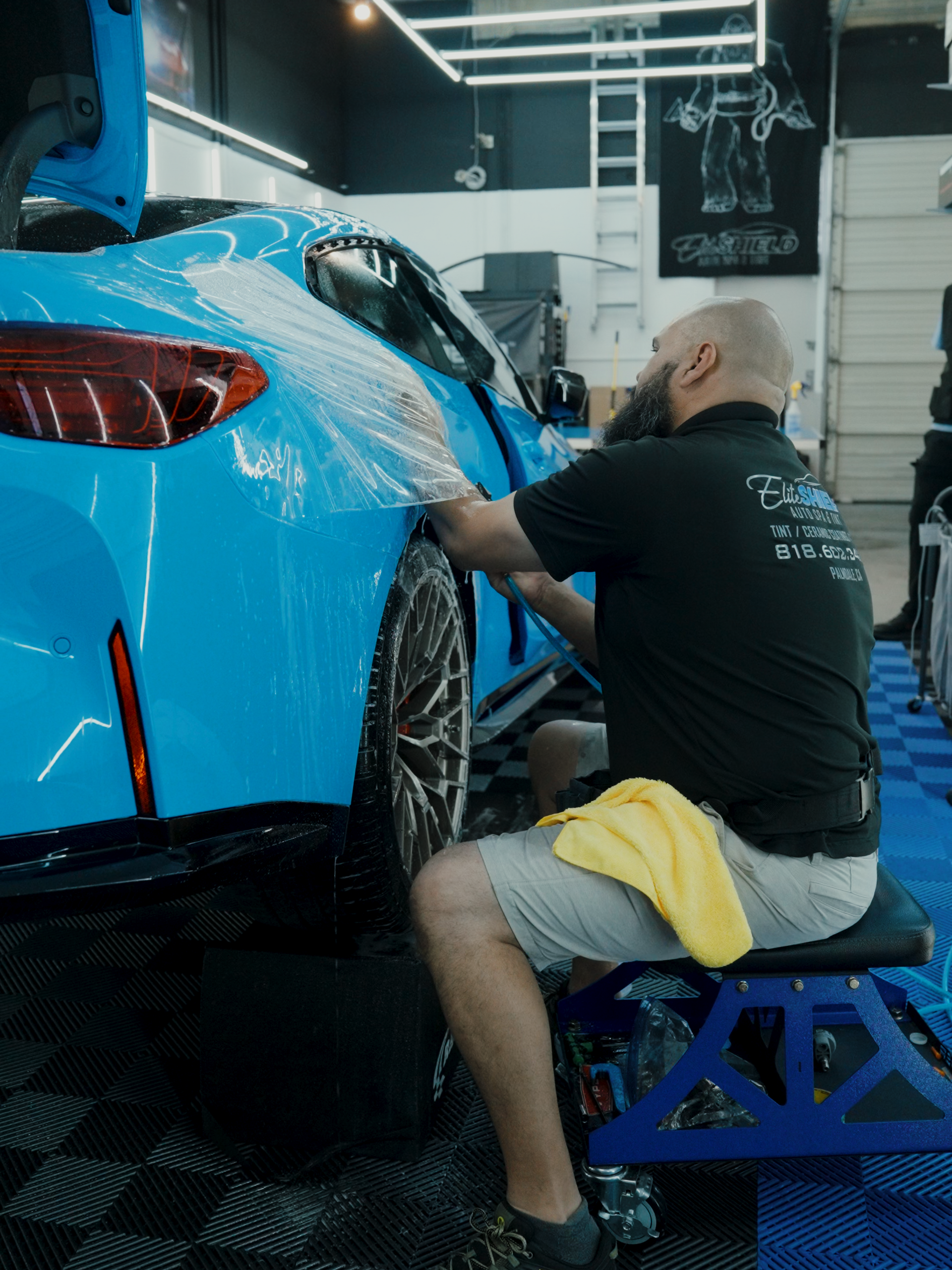 A man is sitting on a stool working on a blue car