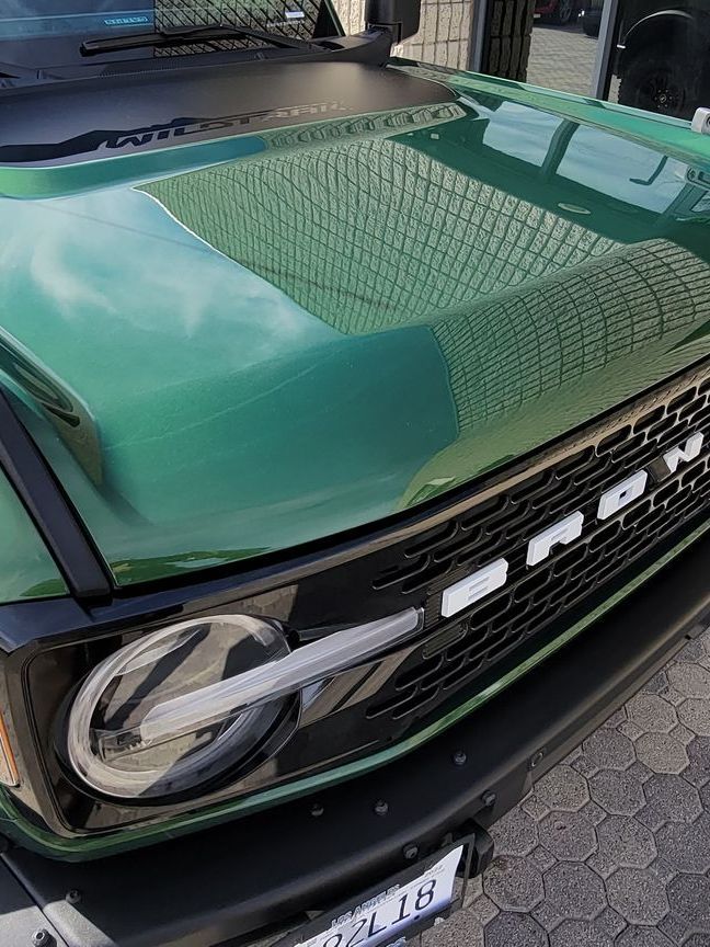 A green ford bronco is parked on the side of the road.