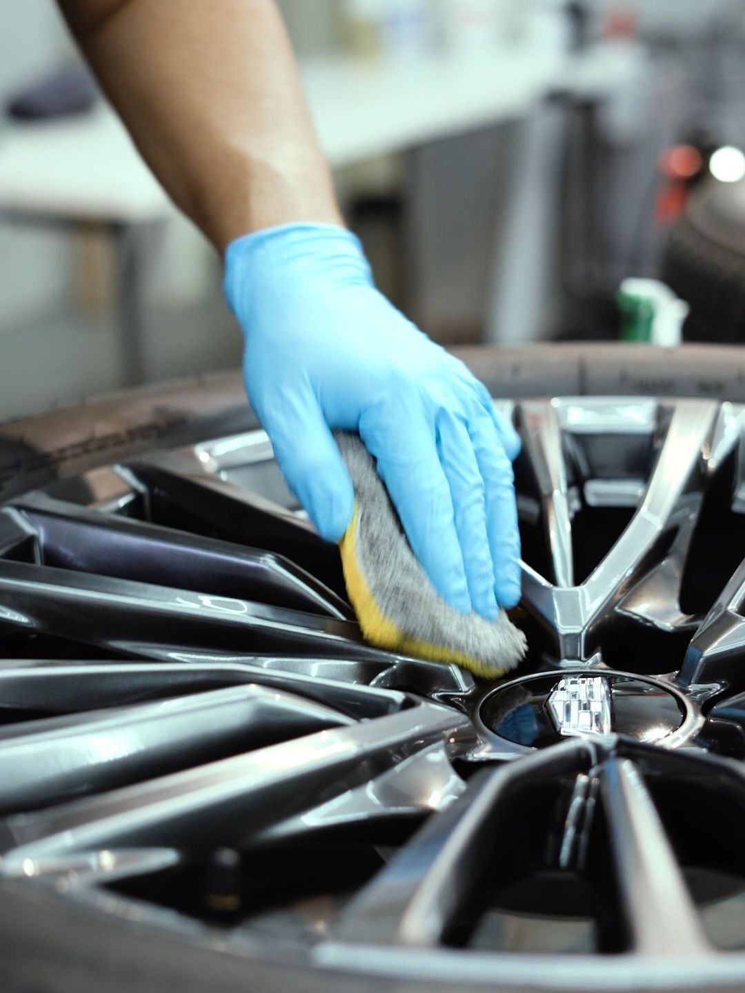 A person wearing blue gloves is cleaning a wheel with a sponge.